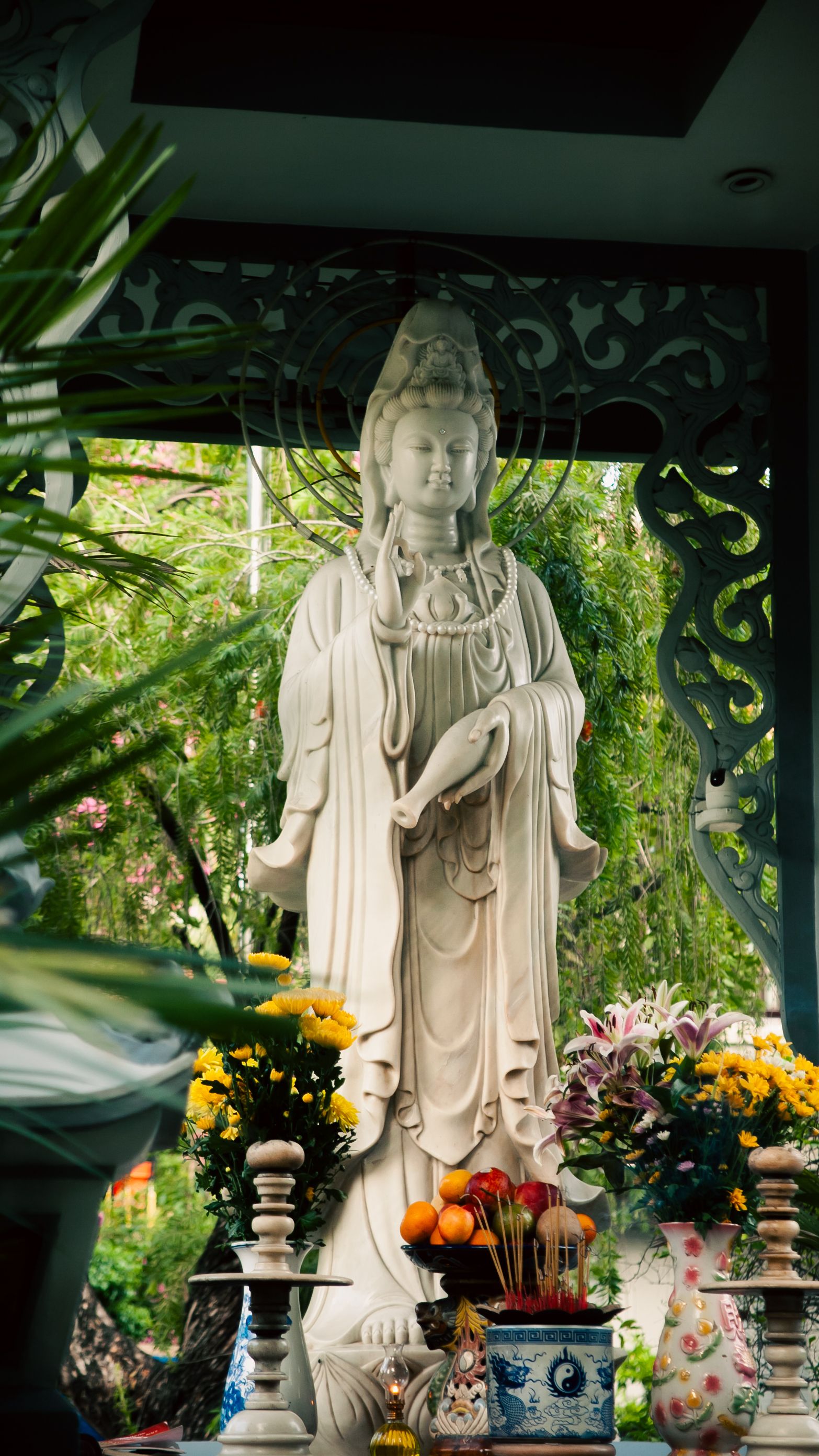 Serene marble Guanyin statue surrounded by colorful flowers in a Vietnamese garden.