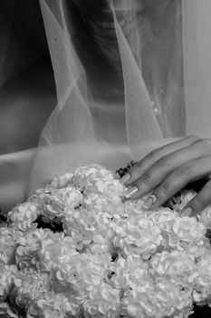 Artistic black and white photo of a bride's hand resting on white flowers, evoking elegance.