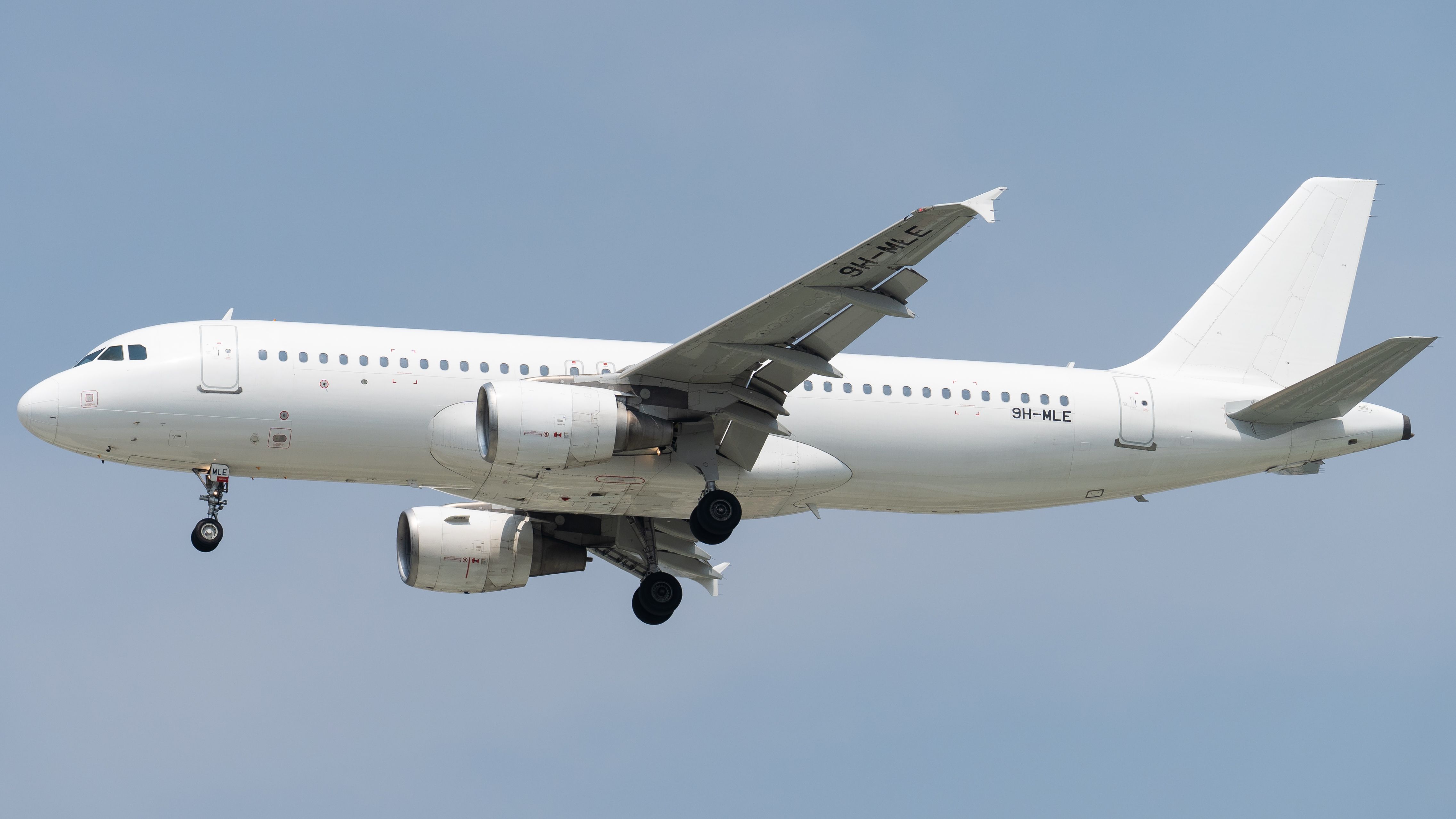 A white commercial airplane flying in the clear blue sky, shot from below.