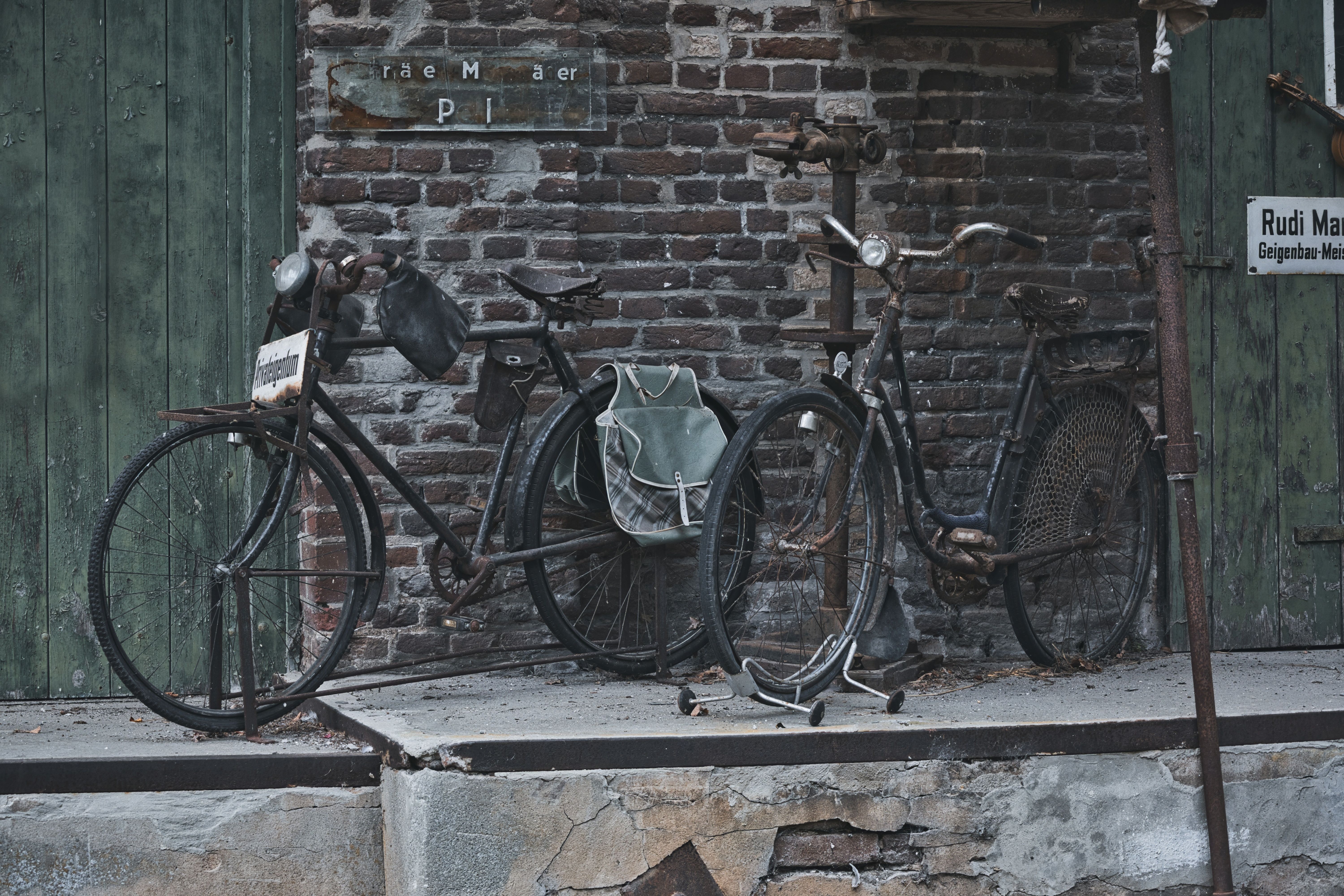 Old, weathered bicycles with rust stand against a rustic brick wall, evoking nostalgia.