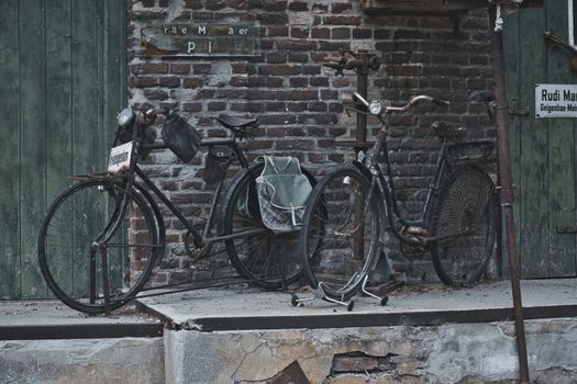 Old, weathered bicycles with rust stand against a rustic brick wall, evoking nostalgia.