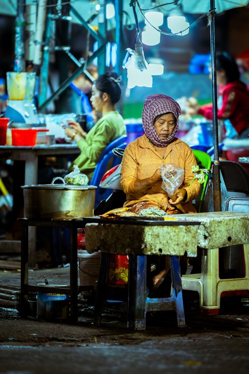 Free An elderly woman vendor prepares food at a bustling Asian night market. Stock Photo