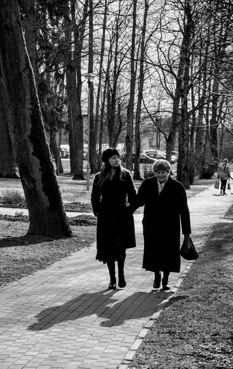 Elegant Young Woman With Aged Mother Strolling In Park On Sunny Day