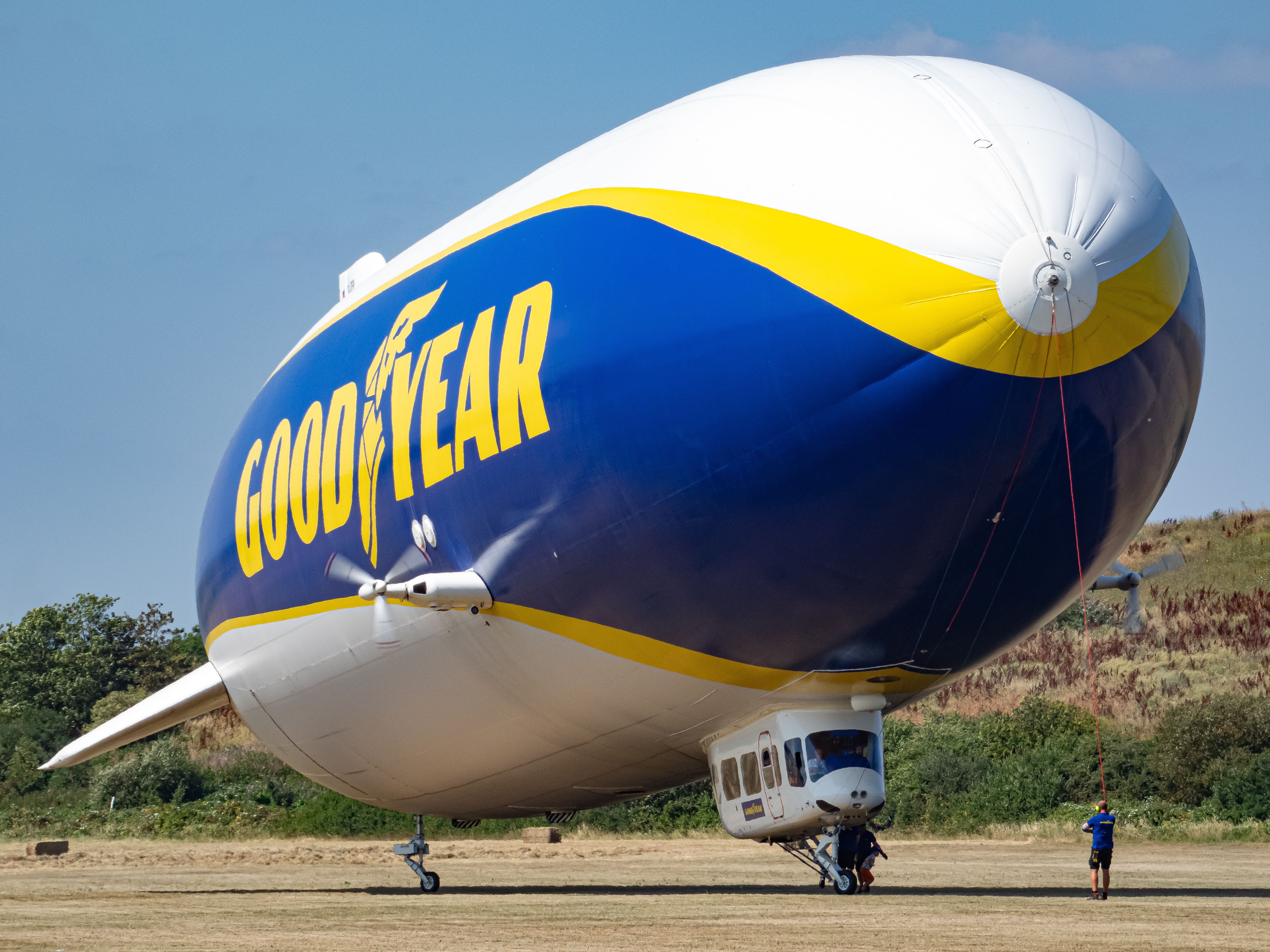 A Goodyear blimp preparing for flight on a clear day, showcasing brand and design.