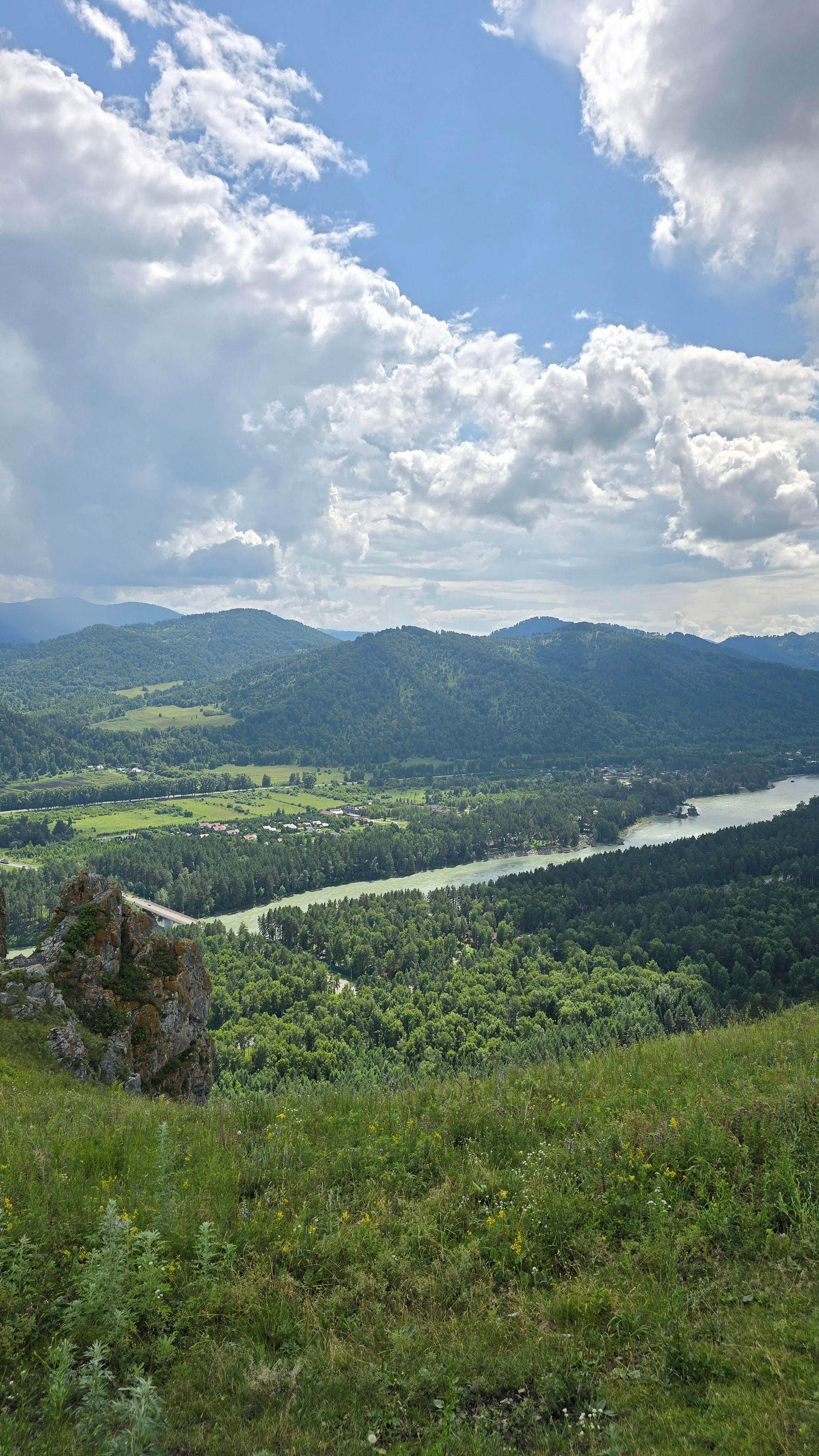 Breathtaking view of mountains and river under a sky filled with clouds, captured from a high vantage point.