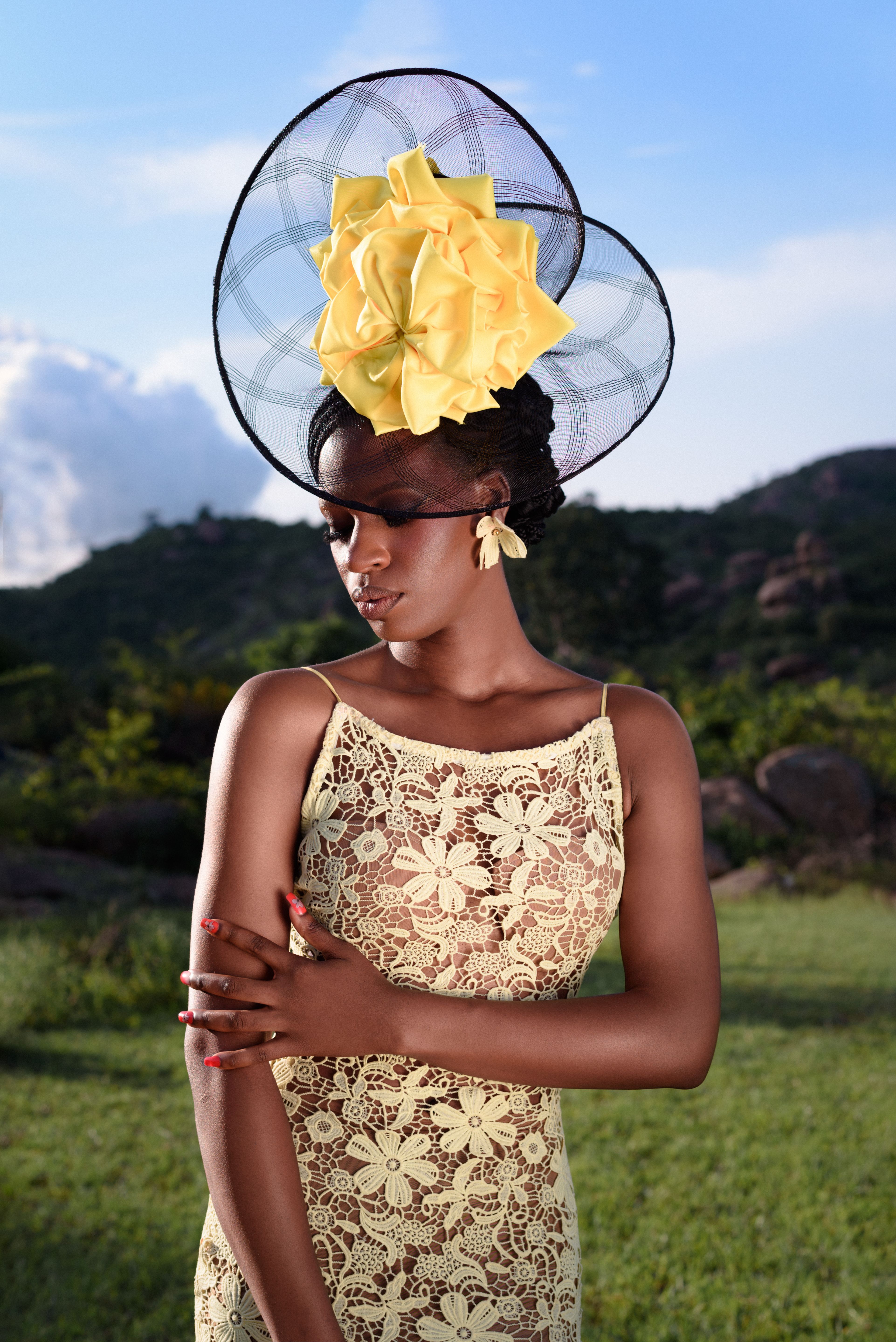 A stylish woman in African fashion with a floral dress and headpiece, set against a Nigerian landscape.