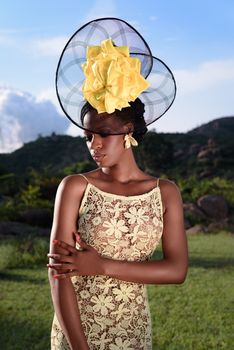 A stylish woman in African fashion with a floral dress and headpiece, set against a Nigerian landscape.