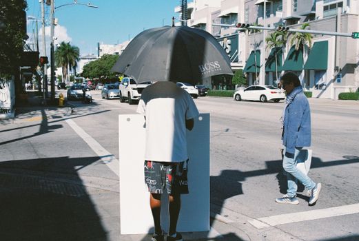 Candid street scene capturing a person with umbrella on a city corner, showcasing urban life.