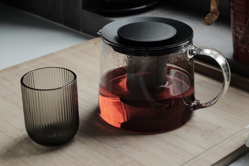 Free Glass teapot with steeping red tea next to a ribbed glass tumbler on a wooden board. Stock Photo