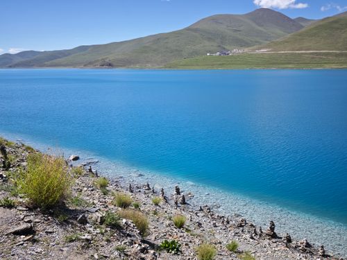 Free Stunning turquoise lake in Tibet with rocky shoreline and distant hills under a clear blue sky. Stock Photo