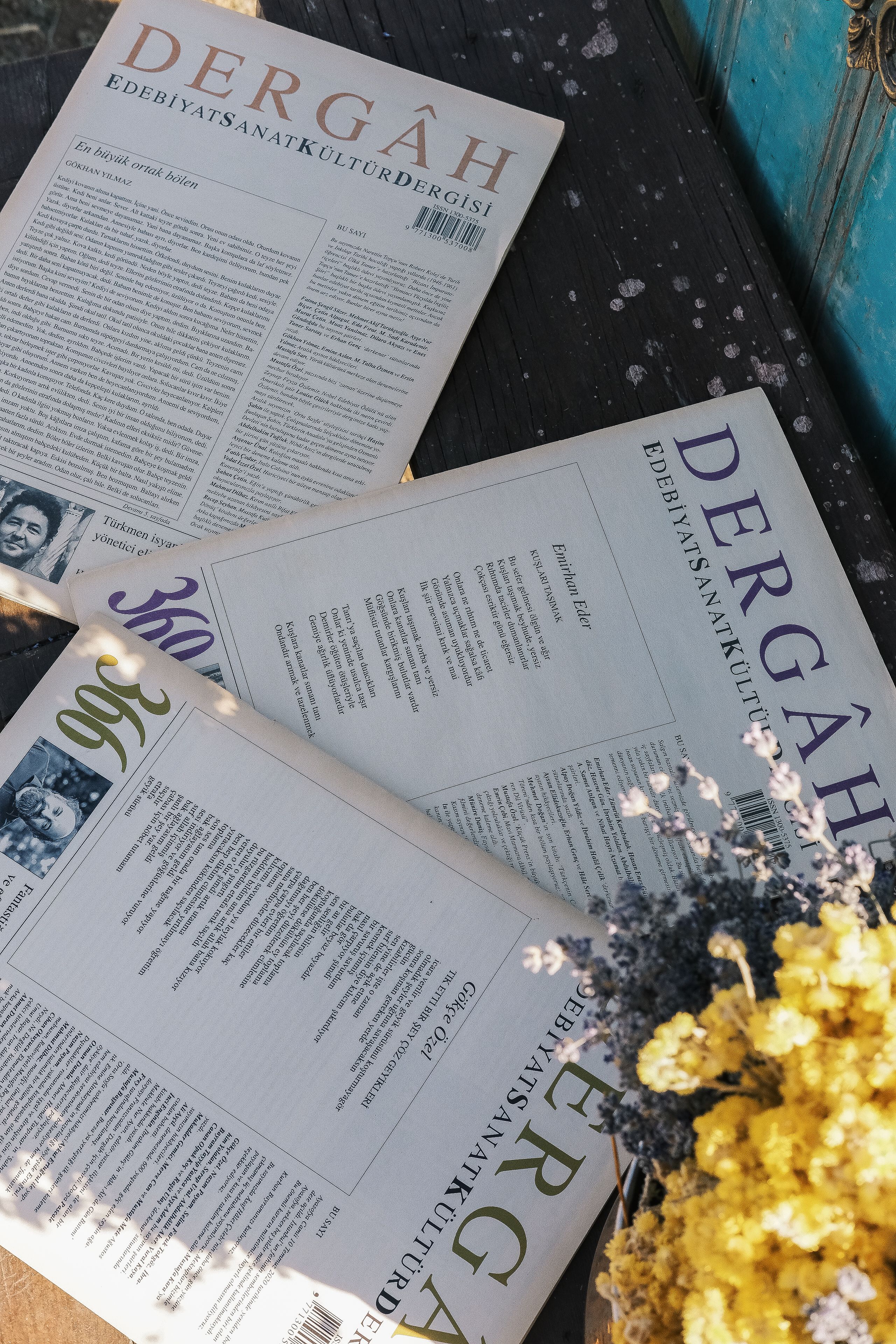 Aesthetic flat lay of Dergah magazines with a bouquet of yellow flowers on a wooden surface.
