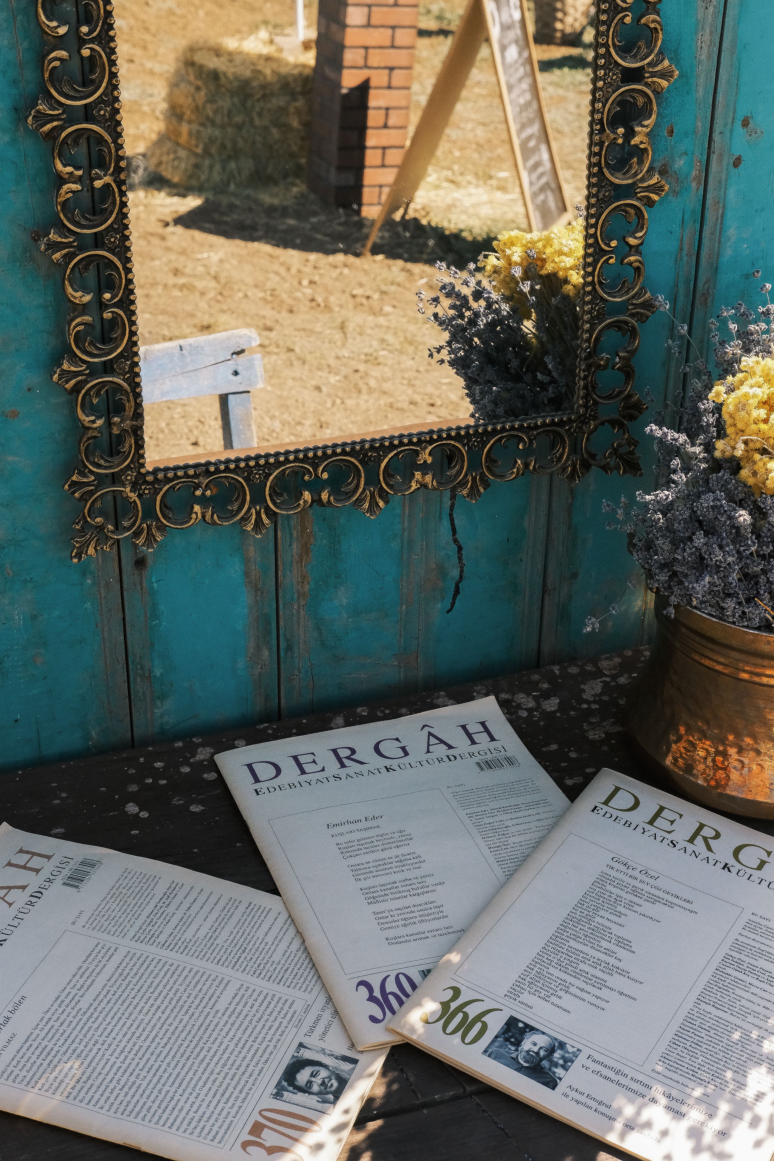 Rustic setup with a vintage mirror, decorative flowers, and Dergah magazines.