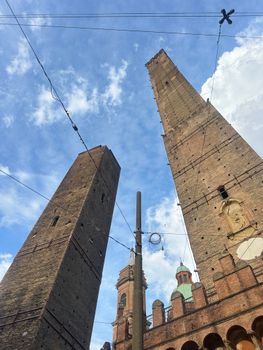 Dynamic view of Bologna's iconic leaning towers, Torre Asinelli and Torre Garisenda, set against a clear blue sky.