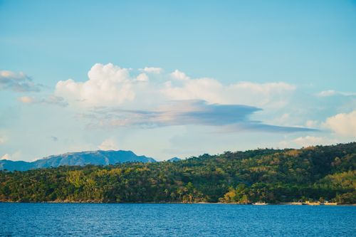 Free Beautiful landscape of a tropical island with lush greenery and calm sea under a vibrant blue sky. Stock Photo