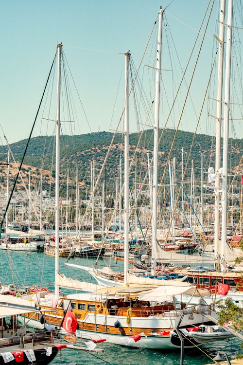 Free Colorful sailing boats docked in a vibrant Turkish marina with scenic hills in the background. Stock Photo