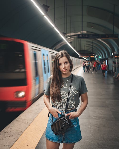 Женщина в серой футболке с круглым вырезом и синей джинсовой юбке стоит возле поезда в метро