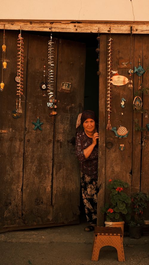Free An elderly woman peeking through a rustic doorway decorated with traditional ornaments. Stock Photo