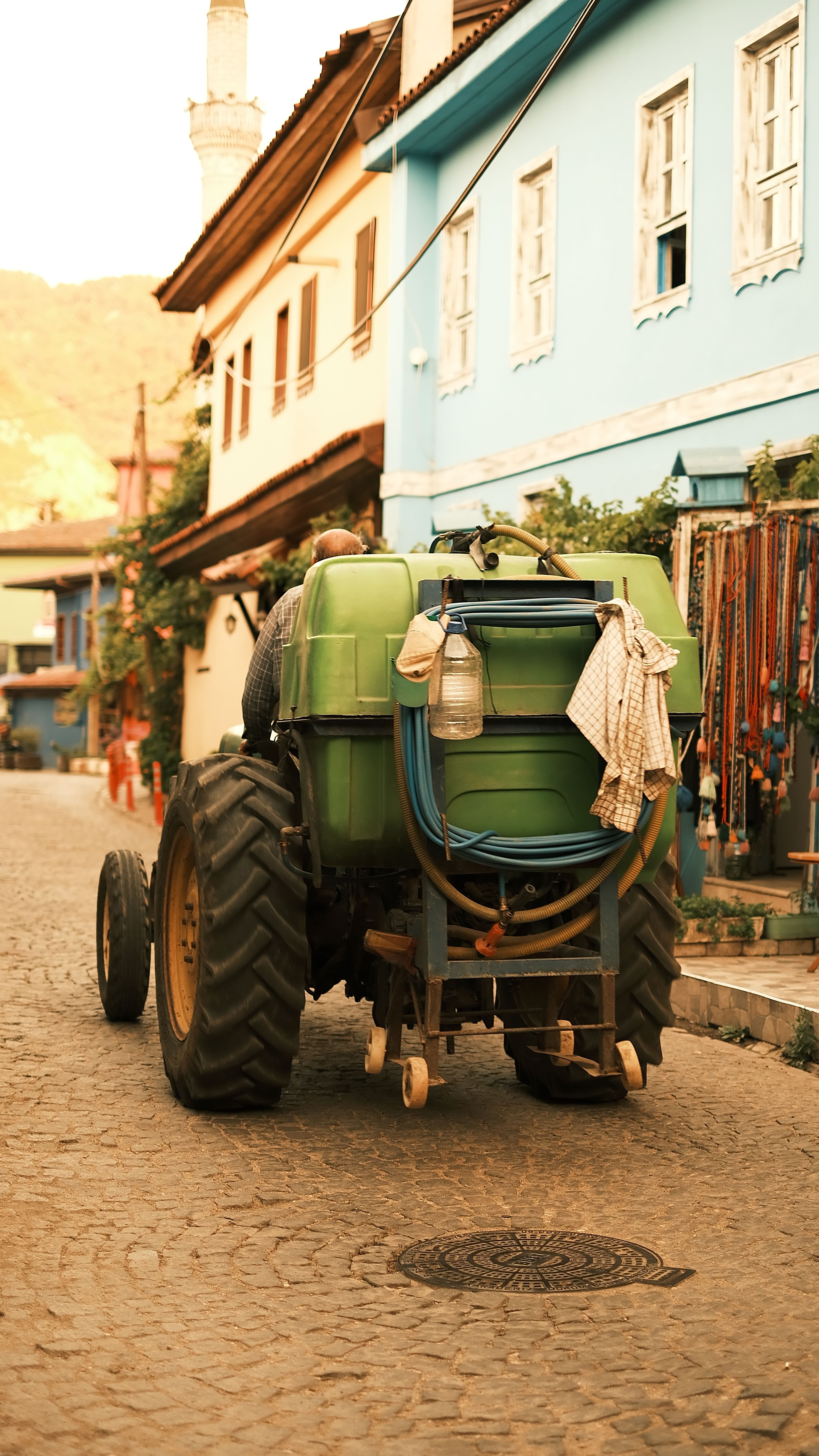 A green tractor on a cobblestone street in a vibrant Mediterranean town at sunset.