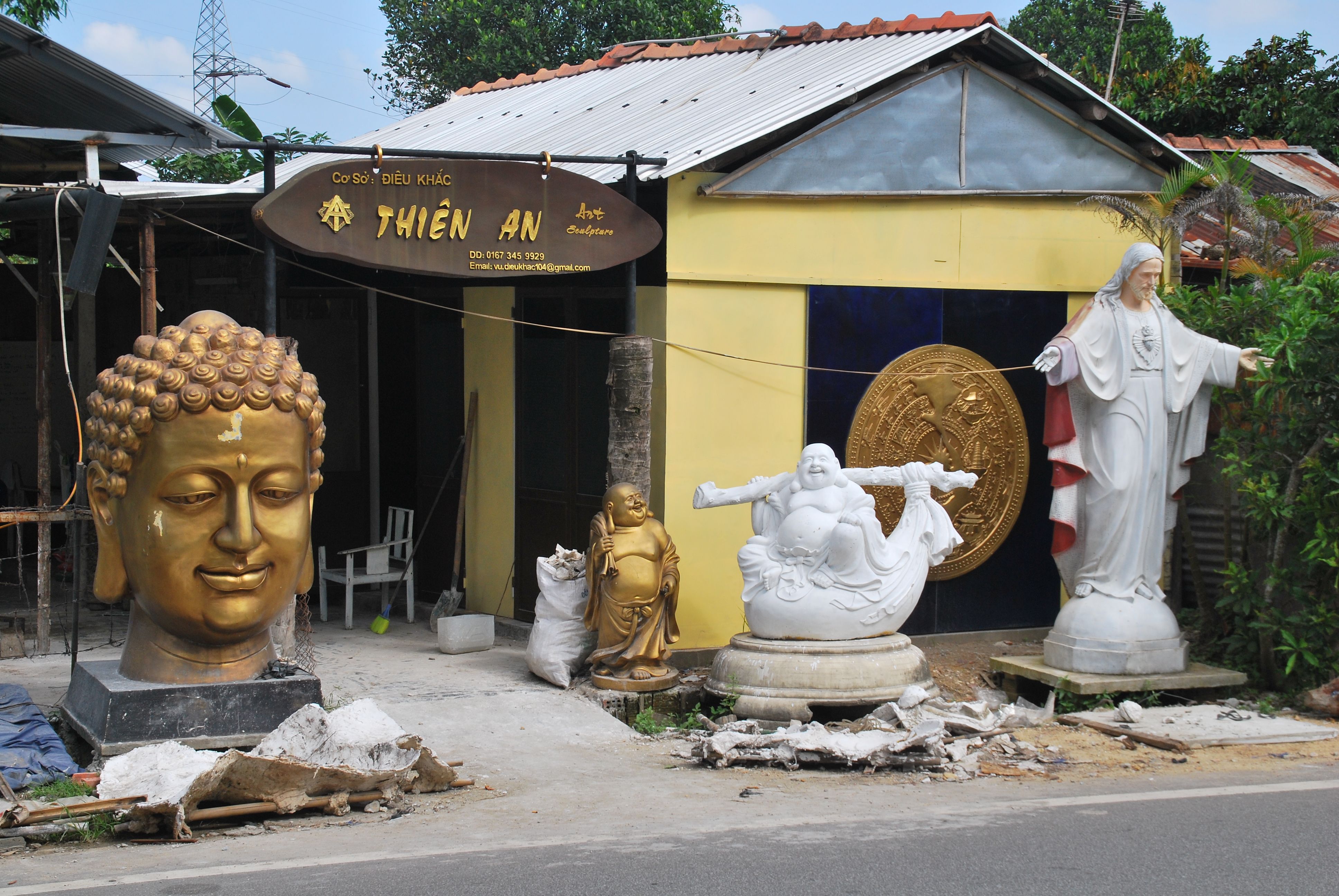 Outdoor display of Buddha and religious statues outside a sculpture workshop.