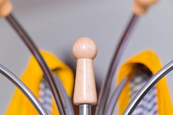 Détail d'une patère en bois sur un portemanteau chromé, ciré jaune en arrière-plan flou