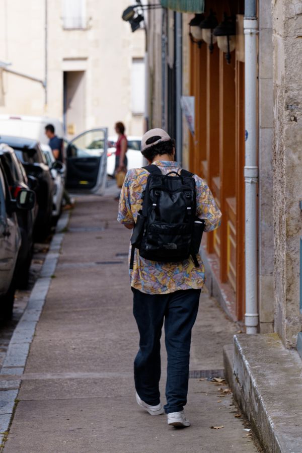 Un homme avec un sac à dos marche dans une ruelle étroite d'un village français
