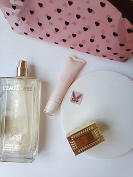 A stylish flat lay of perfume, lip gloss, makeup case, and jewelry on a white surface.