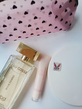 Elegant arrangement of perfume, cosmetic tube, and chic pink bag with hearts.
