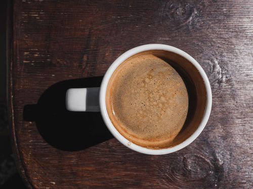Free A close-up top view of a hot espresso served in a white mug on a rustic wooden table, casting a shadow. Stock Photo
