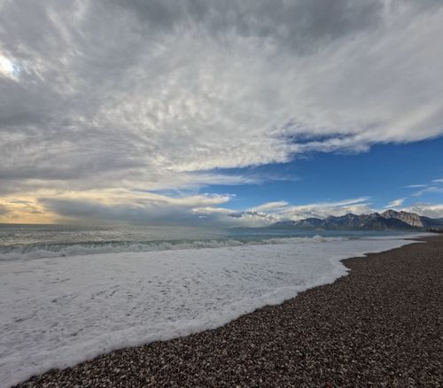 Free Experience the beauty of a pebble beach against majestic mountains and a dramatic sky at golden hour. Stock Photo