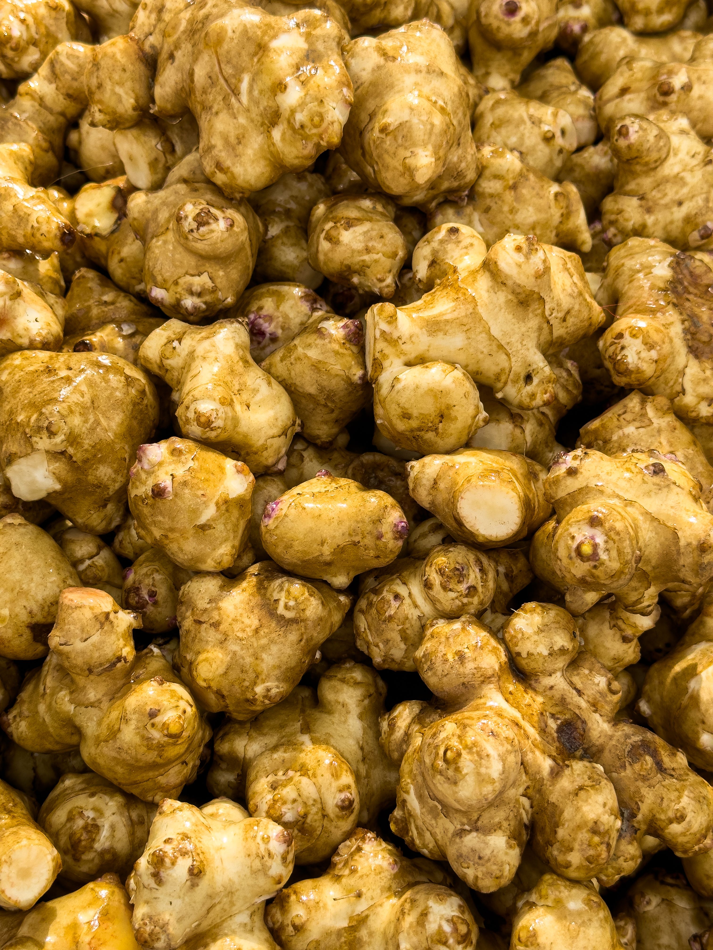 A pile of knobby, thin-skinned sunchokes on a wooden board, some sliced open to show the pale, dense flesh inside.