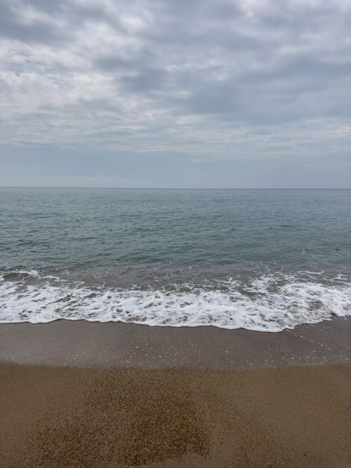 Free A serene coastal scene of Antalya's Mediterranean shore with gentle waves and an overcast sky. Stock Photo