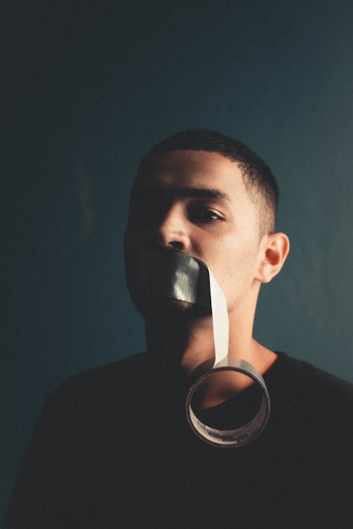 Man in Black Crew Neck T Shirt Covering His Mouth with Masking Tape