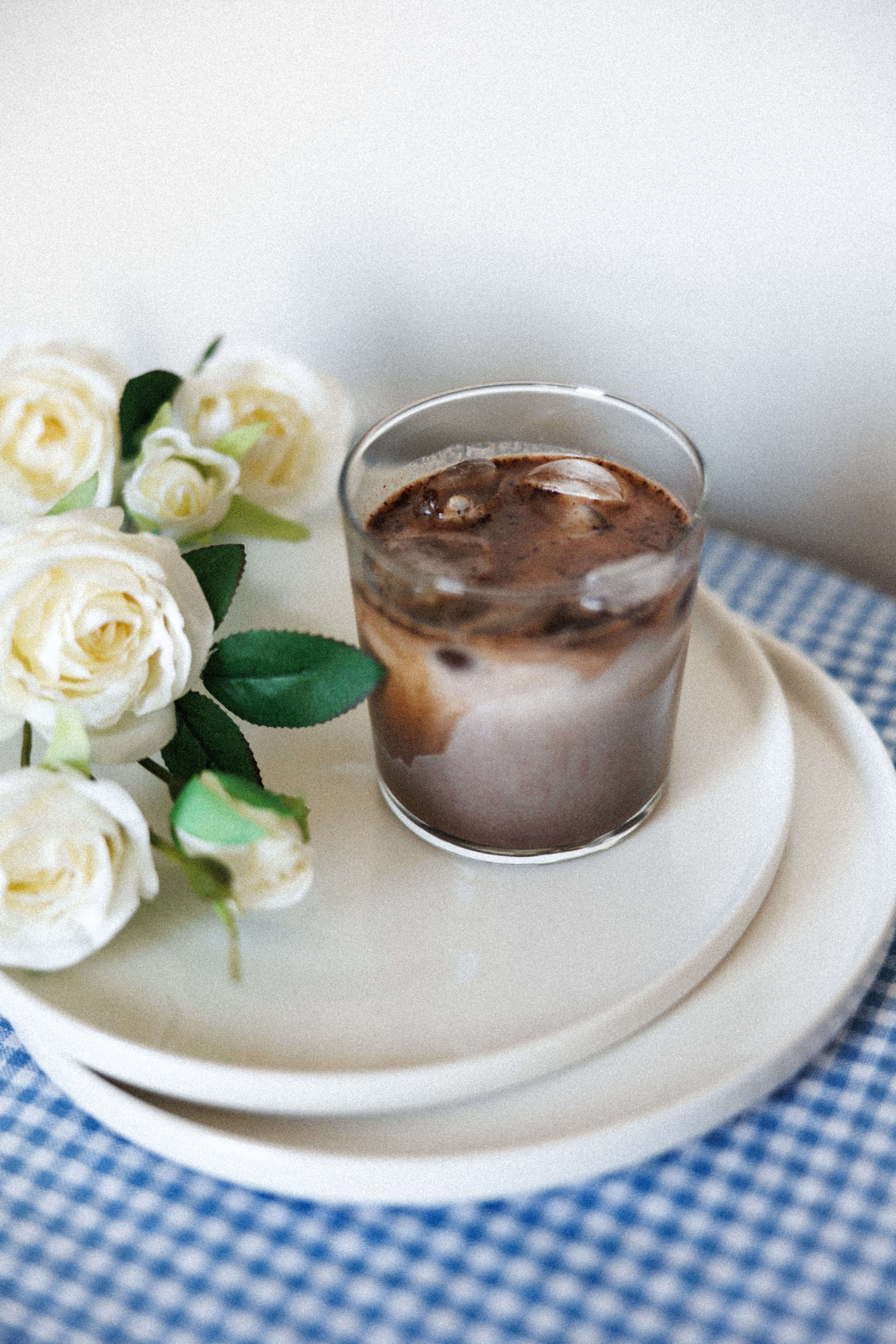 A tall glass of pale amber iced coffee mixed with coconut water, ice cubes, and a lemon wedge on the rim, condensation beading on the glass.