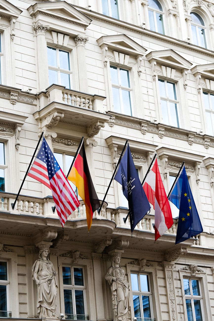 Internationale vlaggen op een klassieke Europese gevel, vertegenwoordigen diplomatie en wereldwijde eenheid.