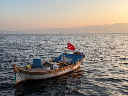 Free A serene fishing boat with a Turkish flag on İzmir Bay at sunset, capturing tranquility. Stock Photo