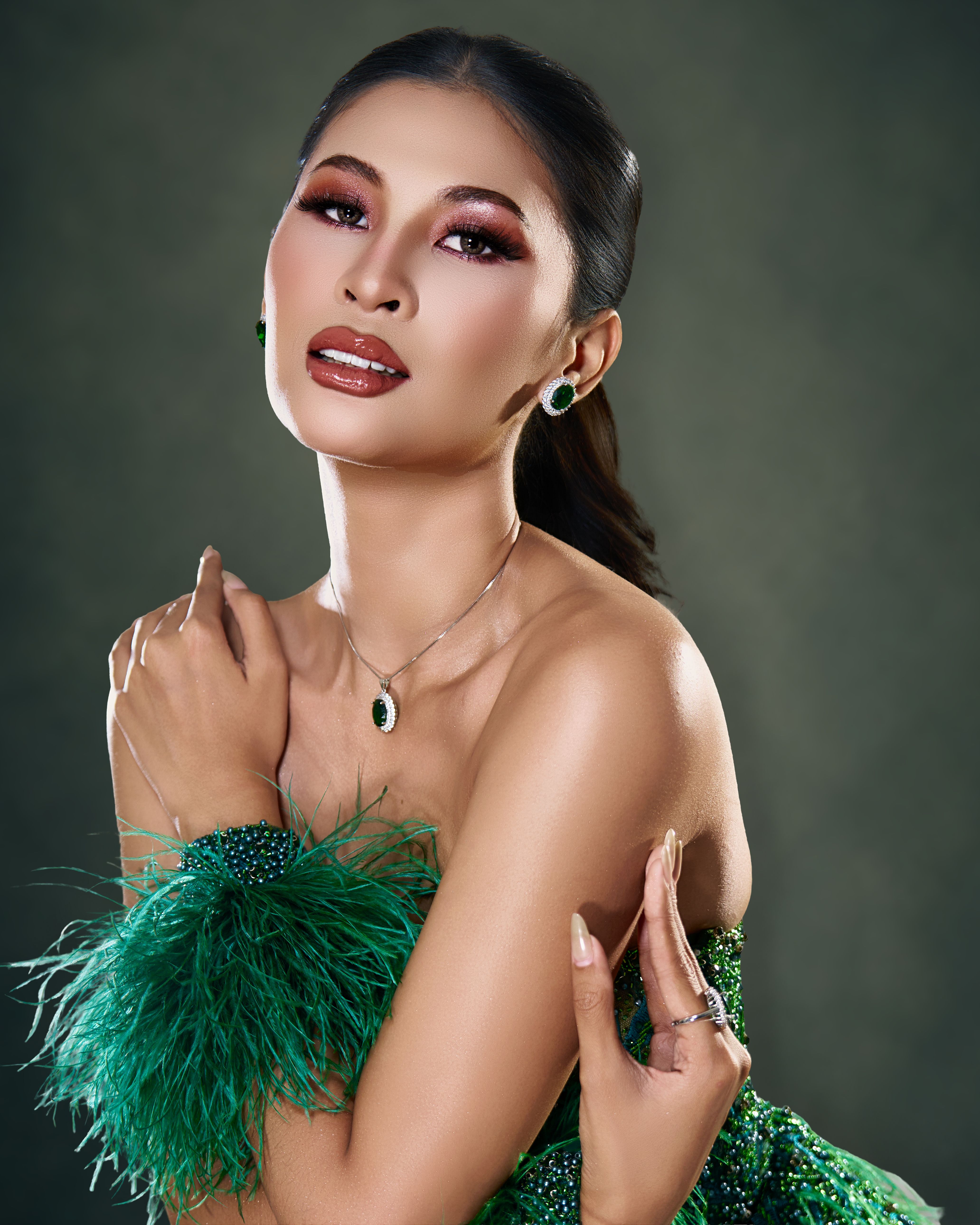A beautiful woman poses elegantly in a green fashion gown and jewelry.