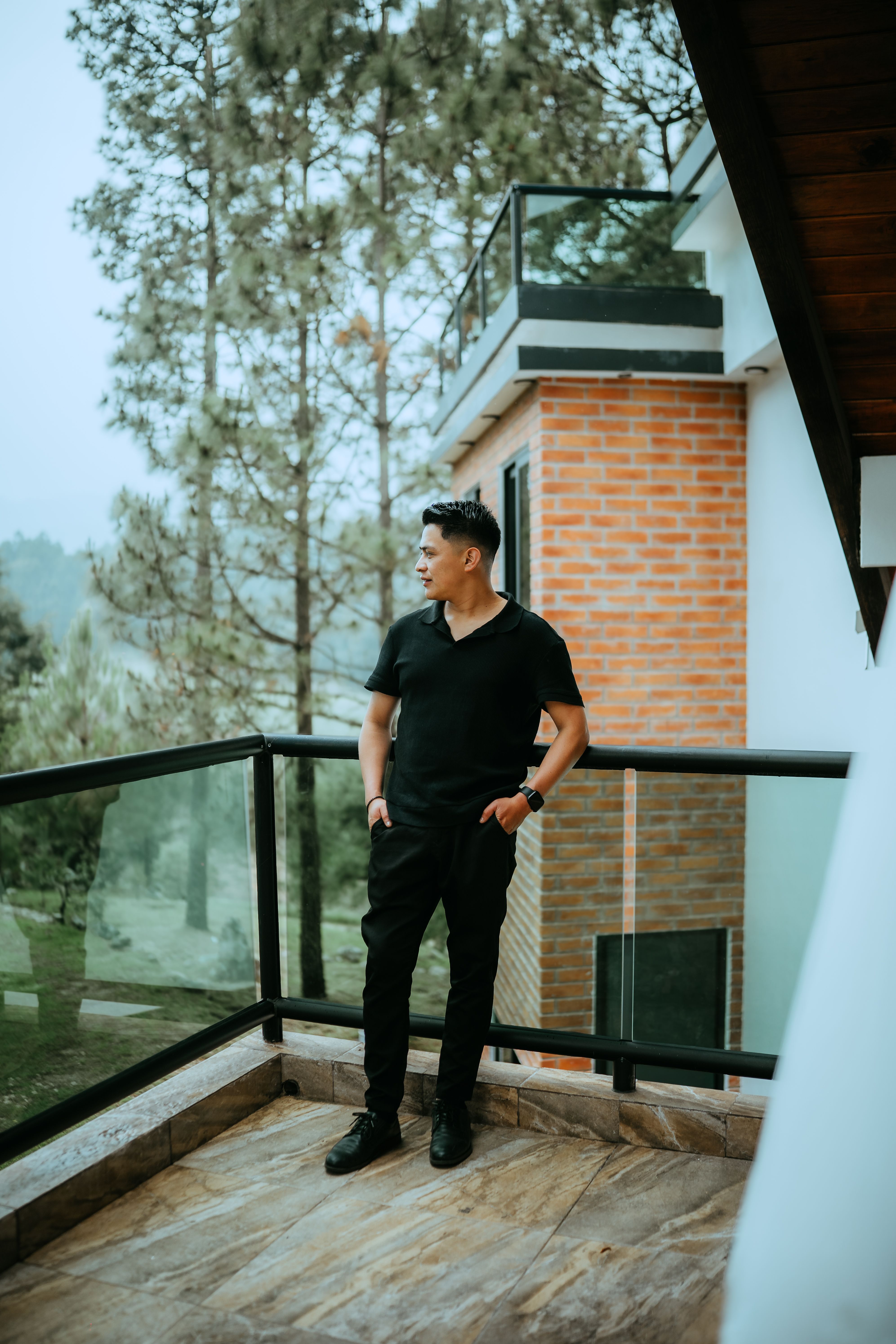 Man in black attire standing on a balcony with forest view in San Cristóbal de las Casas, México.