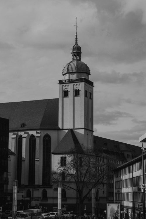 Free A black and white photo of a historic church tower amidst city buildings under cloudy skies. Stock Photo