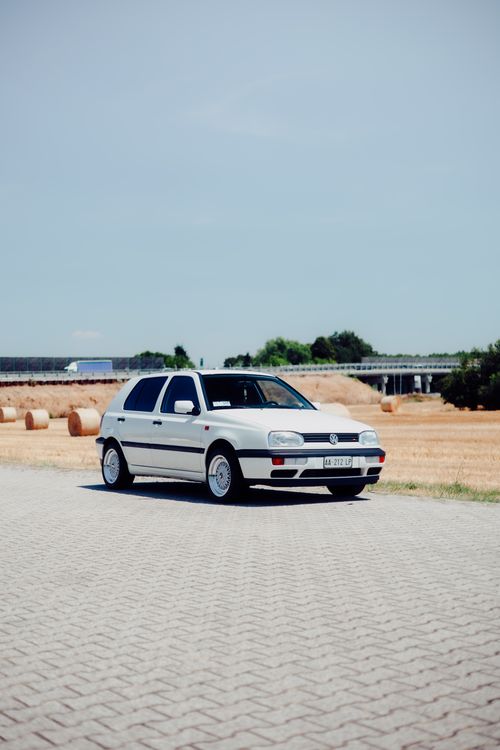 Free A vintage white car parked on a rural road with hay bales and fields in the background. Stock Photo
