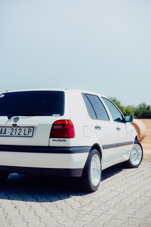 Free Rear view of a white Volkswagen Golf with a blurred scenic background. Stock Photo