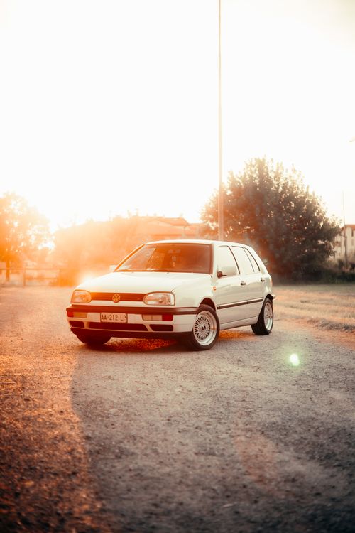 Free A vintage white car illuminated by warm golden sunset on a gravel road outdoors. Stock Photo