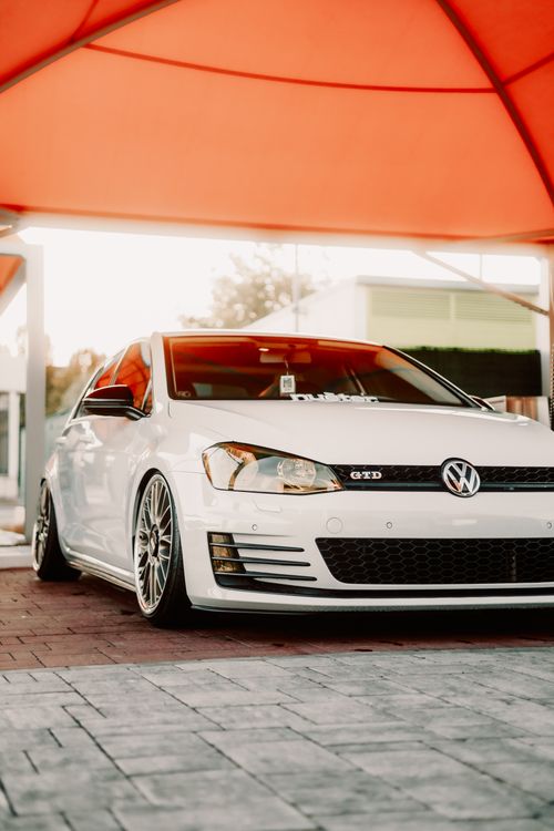 Free A stylish white Volkswagen GTD parked under an orange canopy at sunset. Vibrant, modern car design. Stock Photo