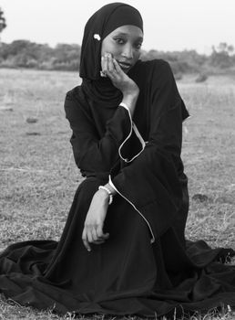 Graceful pose of a woman in a black hijab sitting outdoors in Zaria, Nigeria.