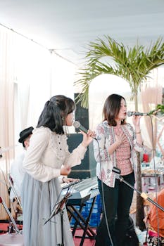 在一场充满活力的室内音乐表演中，两名女子在乐器和棕榈树的装饰下唱歌