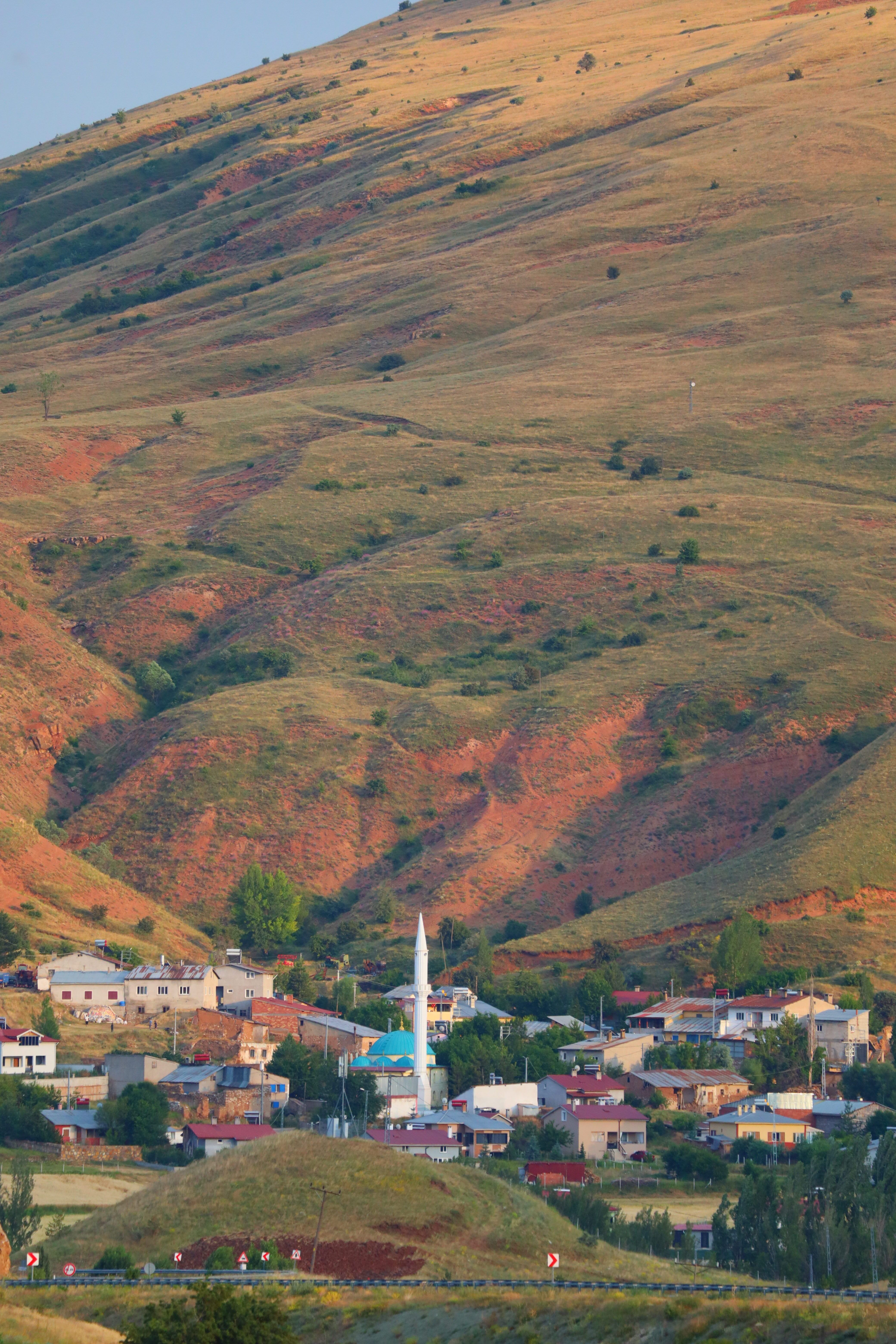Charming rural village with a prominent white mosque set against rolling hills at sunset.