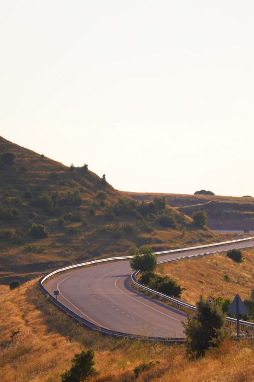 Free Dramatic view of a winding road cutting through sunlit, grassy hills. Stock Photo