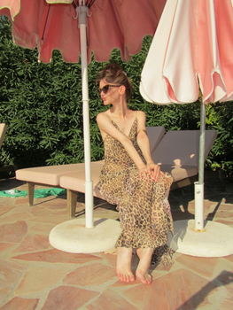 Elegant woman in leopard dress relaxing under a pink umbrella by the pool.