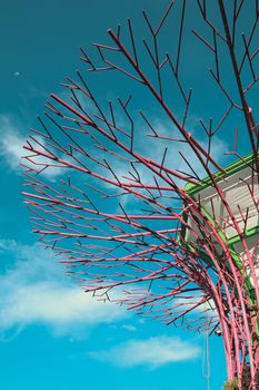 Vibrant sculpture with red branches contrasts against a clear blue sky, capturing modern art's essence.