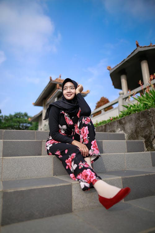 Free Woman in Black Hijab and Pink Floral Pants Sitting on Concrete Stairs Stock Photo
