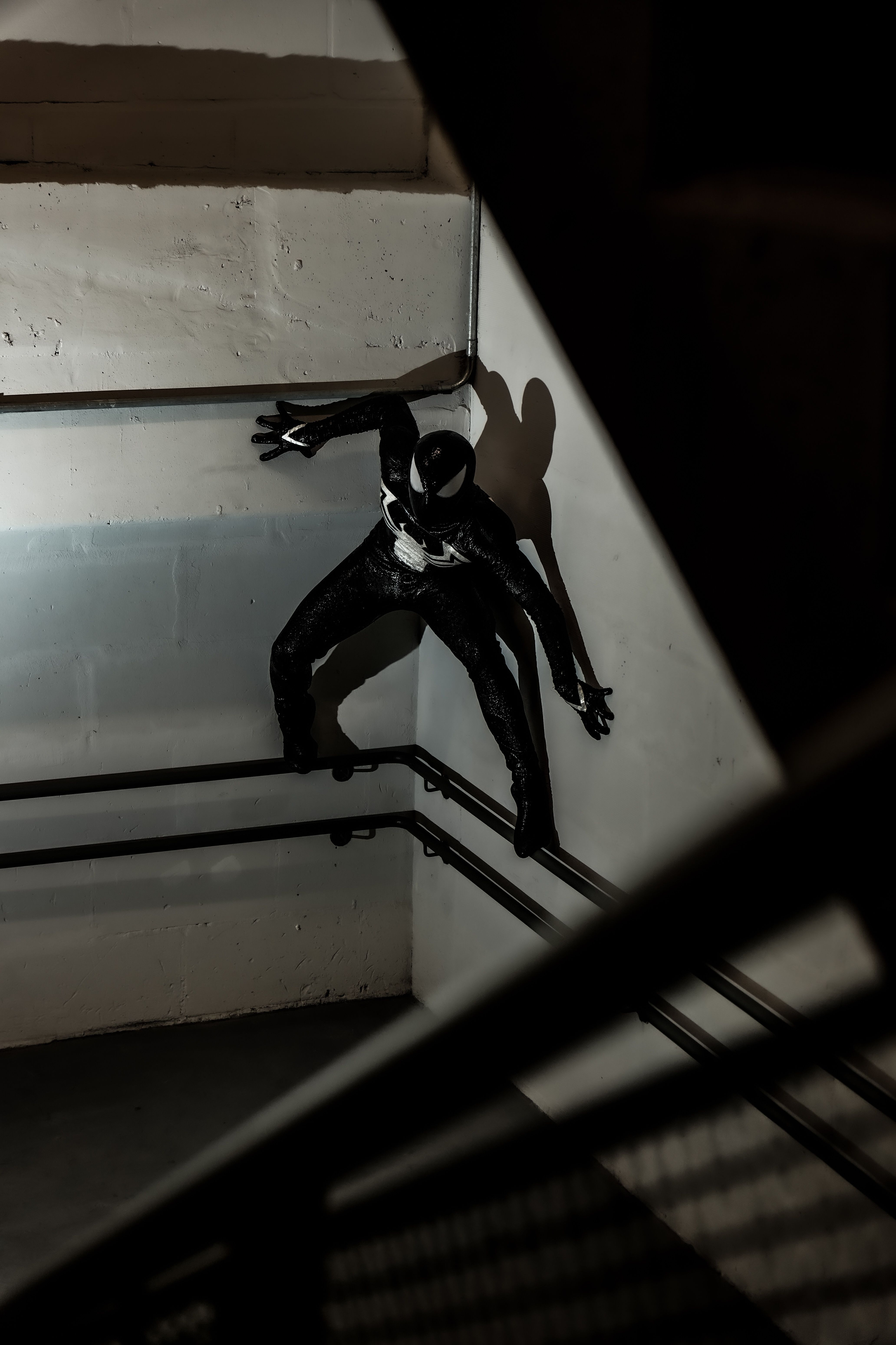 A black-suited figure mimicking Spider-Man climbing in a dimly lit stairwell.